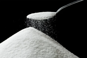 Close-up of a spoon pouring granulated sugar onto a white mound against a black background.