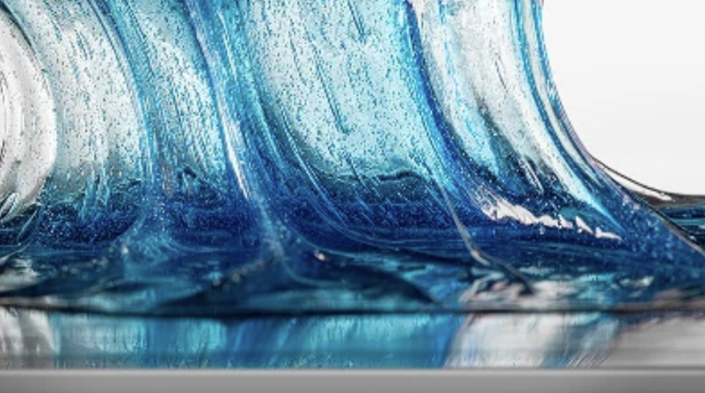 Close-up of blue liquid forming wave-like curves with reflections on a smooth surface.