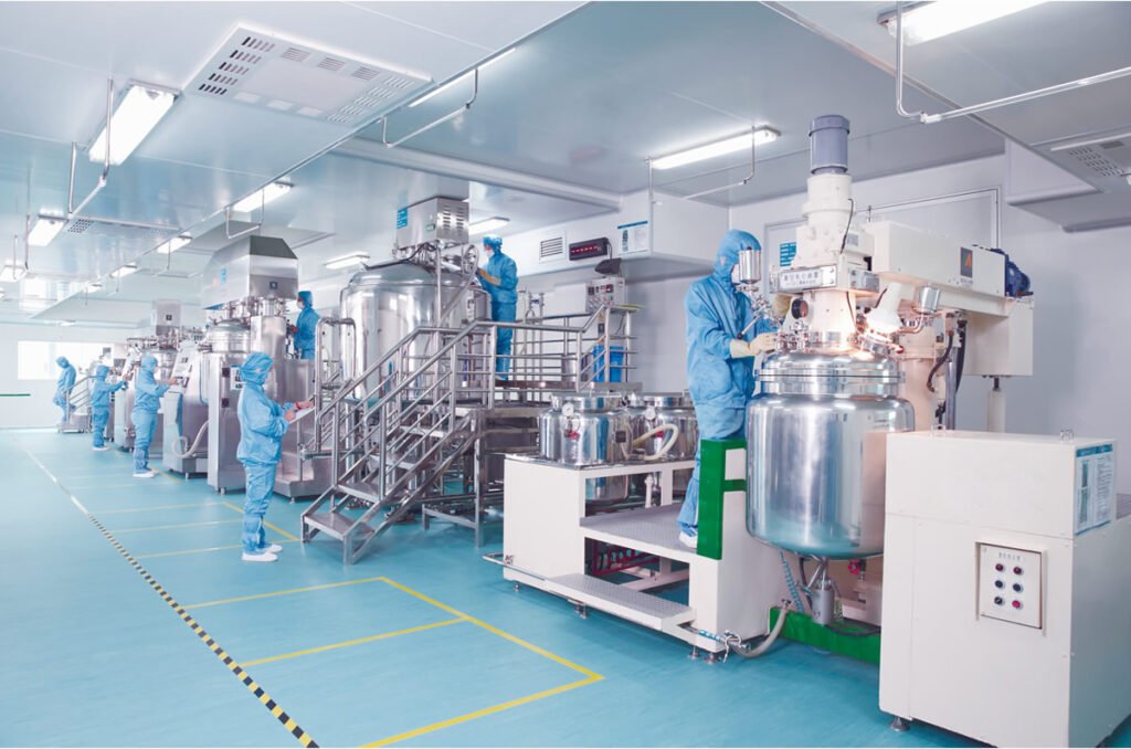 Employees in blue cleanroom suits operate stainless steel pharmaceutical machinery in a bright sterile manufacturing facility