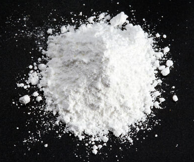 Pile of white flour on a dark surface with scattered flakes around it.