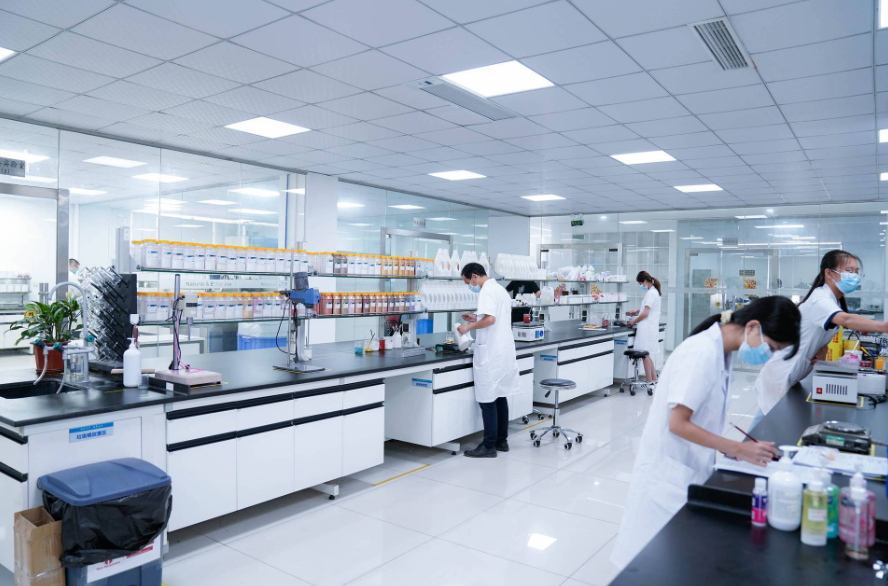 Scientists in lab coats and masks work at benches in a bright, modern research laboratory.