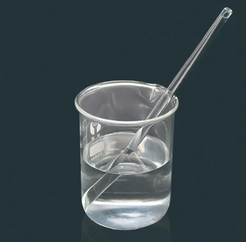 Glass beaker with clear liquid and a glass pipette resting diagonally inside against a dark background
