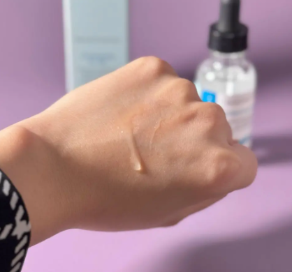 Skin refreshing and softening agent – quartz-chem Close-up of a hand with a small amount of serum swatched on the back of the hand; skincare bottle and box visible in the blurred background.